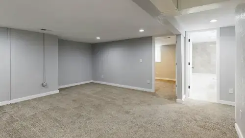 Professional basement remodeling in New Jersey showing a newly finished living area with grey walls and carpet flooring